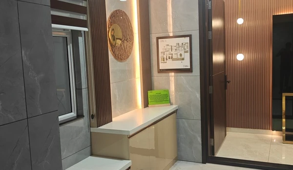 Entrance foyer of the 3 BHK model flat at Nambiar District 25, featuring a shoe console, wall-mounted floor plan, decorative wooden slat paneling, and pendant lighting