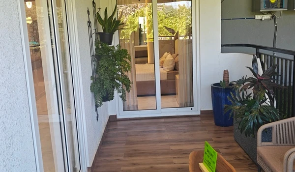 View from the private balcony into the master bedroom at Nambiar District 25 4 BHK model flat, featuring sliding glass doors, vertical garden elements, and wood-finish flooring