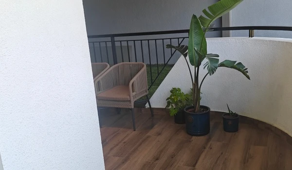 Corner view of the spacious balcony in the Nambiar District 25 4 BHK model flat, featuring a cozy wicker seating nook, large potted plants, and premium wood-finish flooring