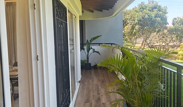 Expansive balcony of the 4 BHK unit at Nambiar District 25, showcasing wood-finish floor tiles, a safety grill gate, and lush green views