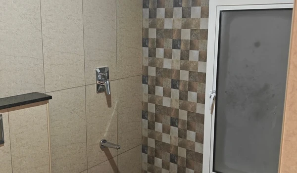 Modern 4 BHK bathroom interior at Nambiar District 25 featuring premium chrome shower fixtures, large beige wall tiles, and a decorative mosaic-patterned accent wall