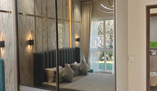 Spacious mirrored sliding wardrobe in Bedroom 1 of Nambiar District 25 4 BHK model flat, reflecting the luxurious green headboard and maximizing natural light