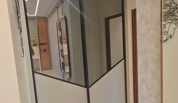 Modern wardrobe in Bedroom 2 at Nambiar District 25 4 BHK model flat, featuring geometric mirrored panels, sleek black framing, and a reflection of the room's decor