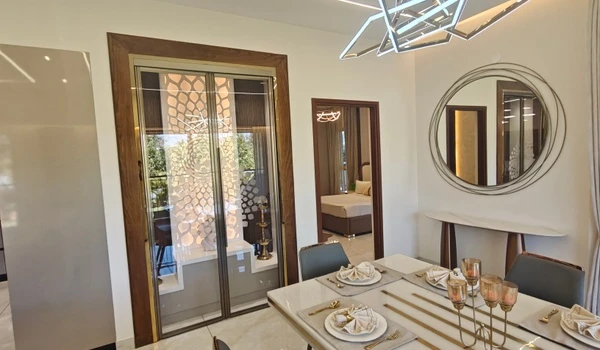 Close-up view of the luxury dining arrangement at Nambiar District 25 4 BHK model flat, featuring a large circular wall mirror, premium tableware, and intricate laser-cut puja room doors