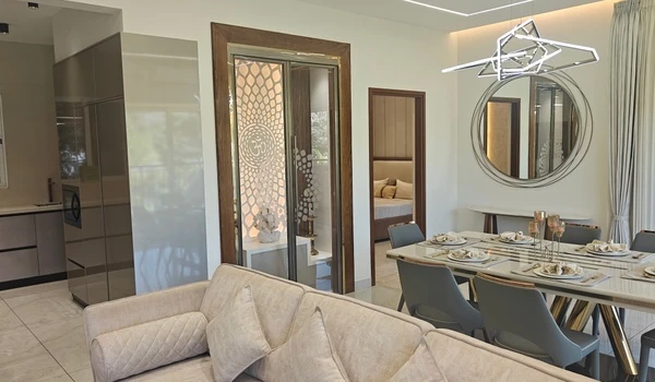 Spacious dining area in the Nambiar District 25 4 BHK model flat, featuring a luxury 6-seater dining table, a decorative circular mirror, and a beautifully designed puja room with laser-cut doors
