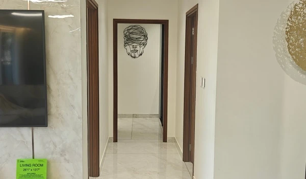 View of the hallway connecting the living room to private bedrooms in the Nambiar District 25 4 BHK model flat, featuring polished marble flooring and a modern wire face wall sculpture