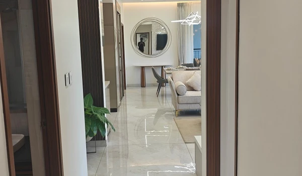 View from the hallway leading to the open-plan living and dining area in the Nambiar District 25 4 BHK model flat, featuring polished marble flooring and modern interior decor