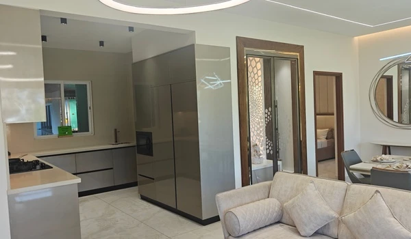 Interior view of the Nambiar District 25 4 BHK model flat, showcasing the transition from the living area to the open kitchen and a decorative puja room with intricate laser-cut doors