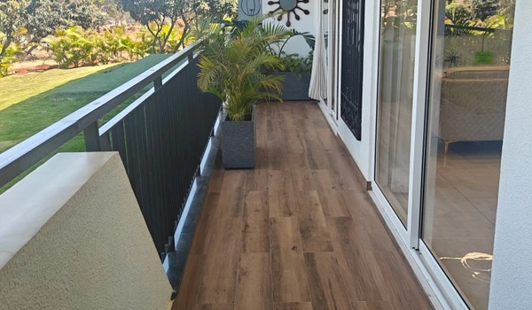 Long view of the spacious 4 BHK balcony at Nambiar District 25, featuring anti-skid wood finish tiles, black metal safety railings, and planters overlooking the landscaped grounds