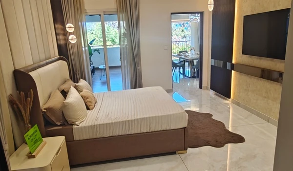 Full overview of the luxurious master bedroom in Nambiar District 25 4 BHK model flat, showcasing the bed placement, TV wall, and direct access to both the private balcony and dining area
