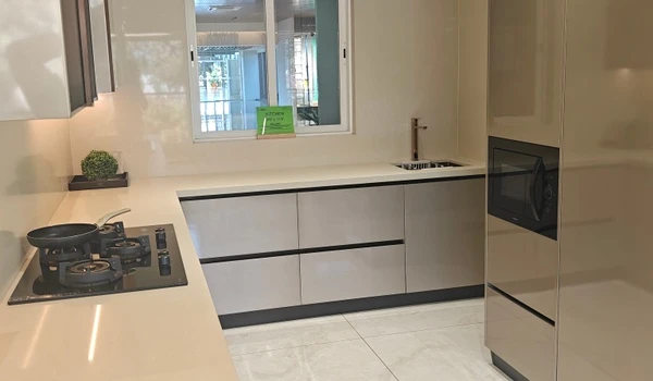 Modern 4 BHK modular kitchen at Nambiar District 25 featuring champagne-toned high-gloss cabinetry, a white quartz countertop with an integrated hob, and a built-in microwave oven