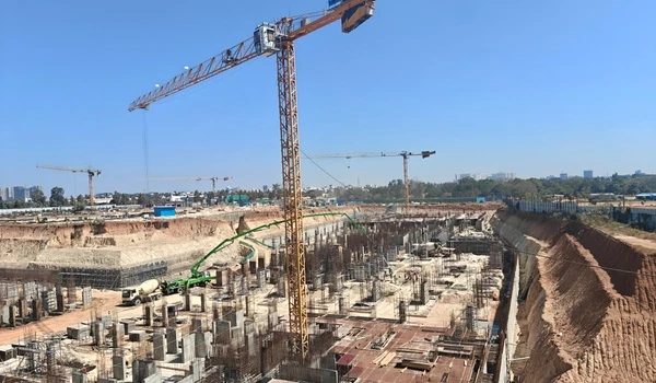 Panoramic view of Nambiar District 25 construction site featuring a large tower crane, foundation reinforcement, and city skyline background