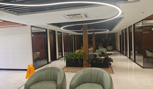 Interior view of Nambiar District 25 sales gallery featuring a distinct S-shaped LED ceiling light, comfortable green armchairs, and private glass meeting cabins