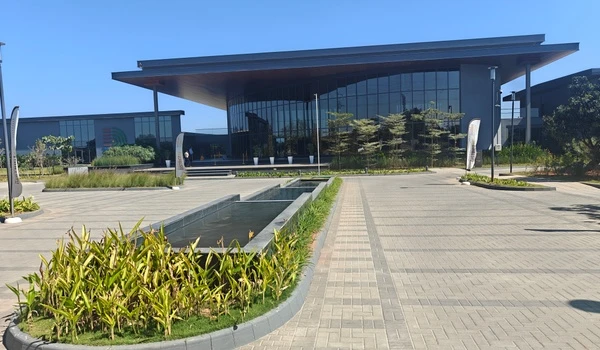 Exterior view of Nambiar District 25 marketing office featuring modern glass architecture, entrance water features, and paved landscaping