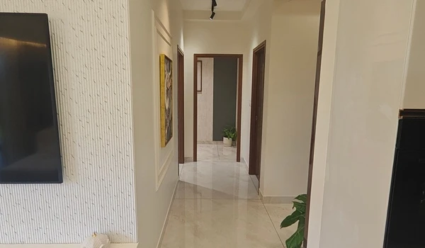 View of the polished marble hallway at Nambiar District 25 model flat, leading to private bedrooms and featuring modern wall art and recessed lighting