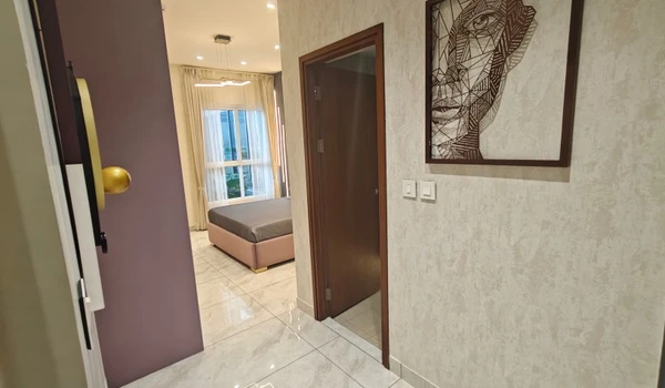 Interior hallway view of Nambiar District 25 model flat leading to a modern bedroom with a large window, featuring marble flooring and contemporary wall art