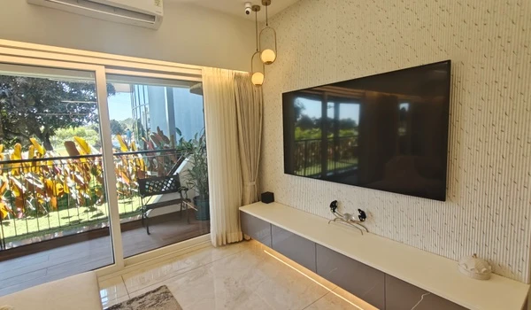 Modern living room media center at Nambiar District 25 featuring a large wall-mounted TV, sleek floating grey cabinetry with under-lighting, and large sliding glass doors leading to a private balcony