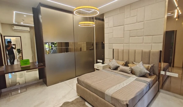 Luxury bedroom at Nambiar District 25 model flat featuring a large floor-to-ceiling mirrored wardrobe, a king-sized bed with an upholstered geometric headboard, and designer circular pendant lighting
