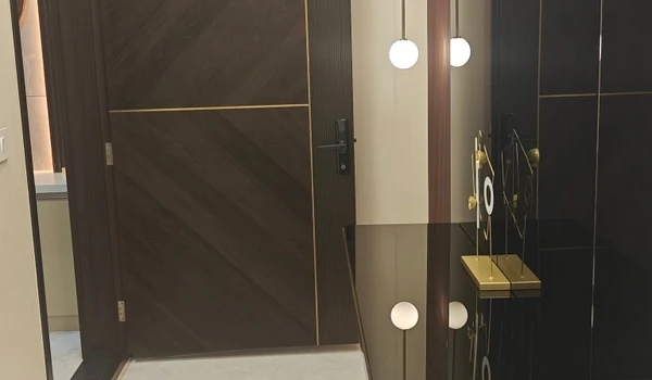 Premium main entrance door of the Nambiar District 25 model flat featuring a dark wood finish with diagonal grain patterns, gold metallic inlays, and a modern digital smart lock.