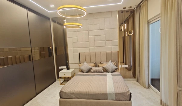 Luxury master bedroom at Nambiar District 25 featuring a king-sized bed with a block-patterned headboard, gold ring pendant lights, a full-height mirrored wardrobe, and sliding balcony doors