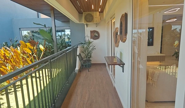Lengthwise view of a spacious private balcony at Nambiar District 25, featuring premium wood-finish flooring, a modern wooden ceiling with integrated strip lighting, and a safe black metal railing overlooking lush gardens