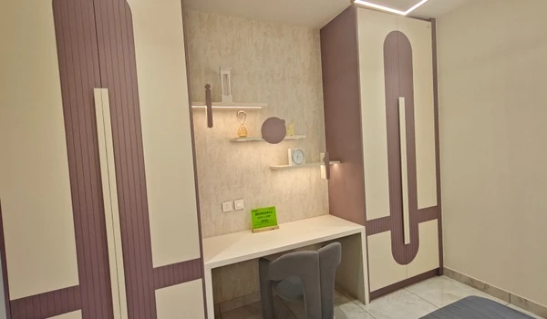 Modern study nook and wardrobe design in a Nambiar District 25 model flat, featuring sleek lavender and white cabinetry, floating shelves with integrated lighting, and a minimalist desk