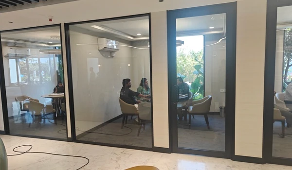Row of glass-enclosed meeting cabins at Nambiar District 25 sales gallery, showing clients and sales staff engaged in private discussions
