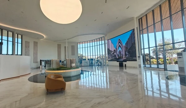 Grand interior view of Nambiar District 25 sales gallery featuring a massive circular ceiling light, curved LED display screen, and polished marble flooring