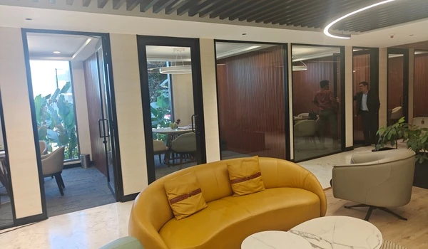Interior view of Nambiar District 25 sales gallery featuring private glass-walled meeting cabins, a comfortable lounge area with a yellow sofa, and modern interior design